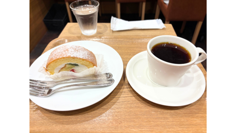 カフェで提供されたロールケーキとホットコーヒー。ロールケーキの皿にはフォークが2本添えられ、シェアを想定した心配りが感じられる。