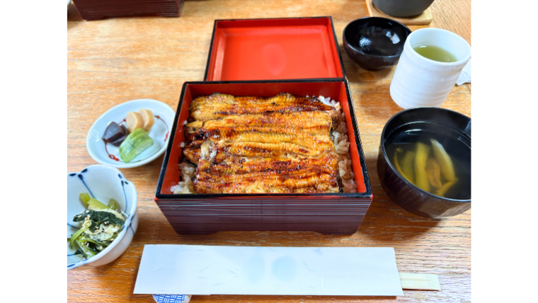 土用の丑の日に食べるうな重の写真。漆塗りの重箱に盛られた香ばしい鰻の蒲焼きとご飯、吸い物、漬物、小鉢、そして温かいお茶が並んでいる。