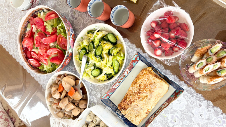 実家で母が用意してくれた野菜中心の手料理。サラダ、煮物、卵焼き、いちごなど、彩り豊かな料理がテーブルに並んでいる。